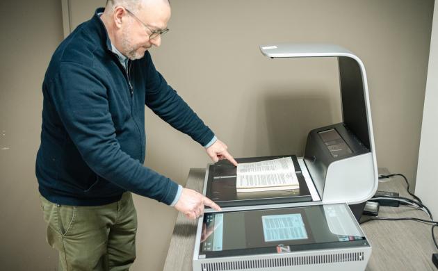 Leeszaalbezoeker gebruikt boekscanner om spread van boek in te scannen.