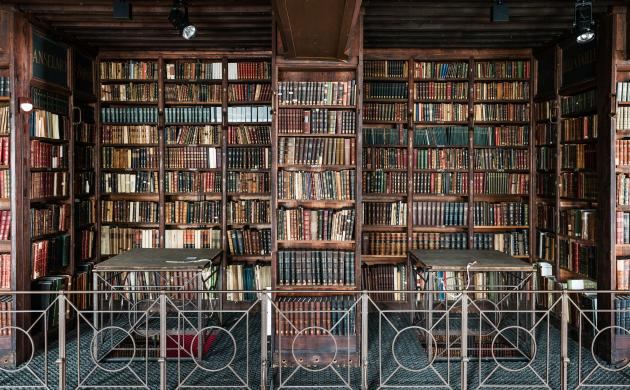 Zicht op bovenverdieping Nottebohmzaal met boekenkasten, twee leestafels en gietijzeren gaanderij