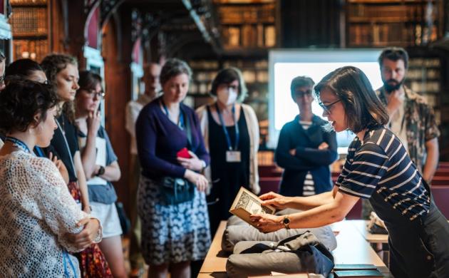 Een groep mensen luistert naar een vrouw die vertelt over een oud boek